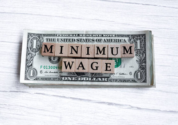 Minimum wage word written on wood block with American Dollar-bills. Directly above. Flat lay. Employment concept.